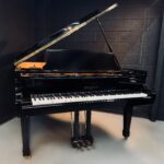 Shiny black grand piano with open lid in a dark studio, brand Sherman Clay visible on the fallboard.