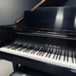 Close-up of a glossy black K. KAWAI grand piano with the lid open and white and black keys visible