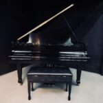 Black grand piano with open lid in a dark room, reflection on the polished surface, matching bench in front